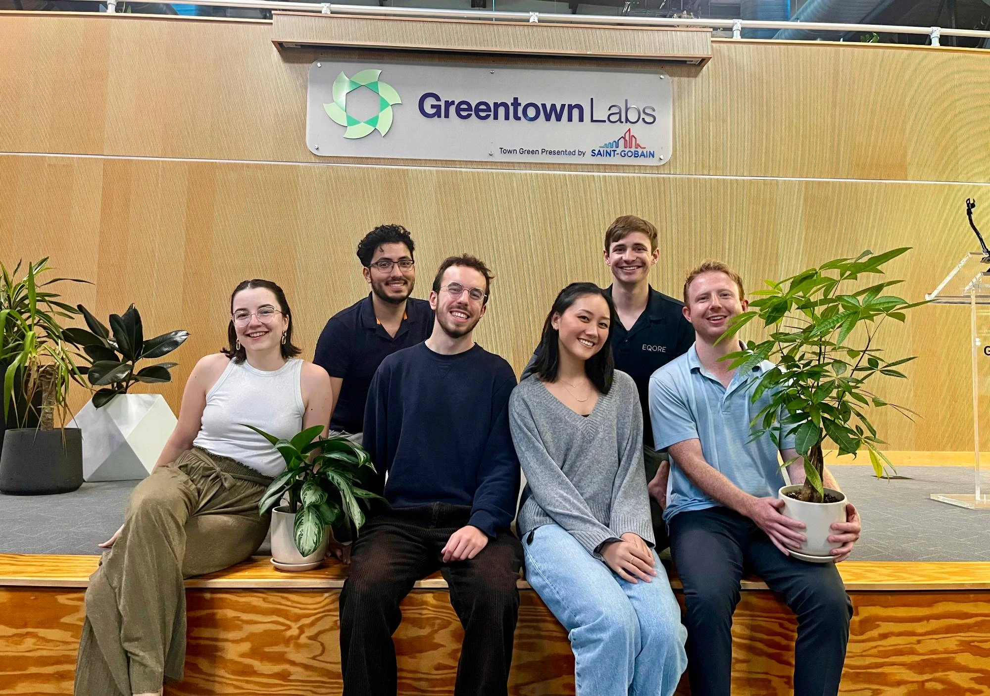 Six members of the EQORE team sitting together under the Greentown Labs sign in Somerville